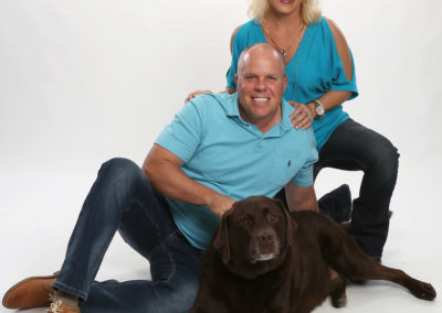 A husband and wife pose for a photo with their dog.